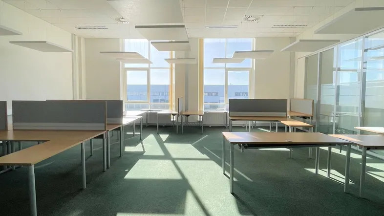 Heller Großraumbüro mit mehreren Arbeitsplätzen, grünem Teppichboden und großen Fenstern für viel Tageslicht.