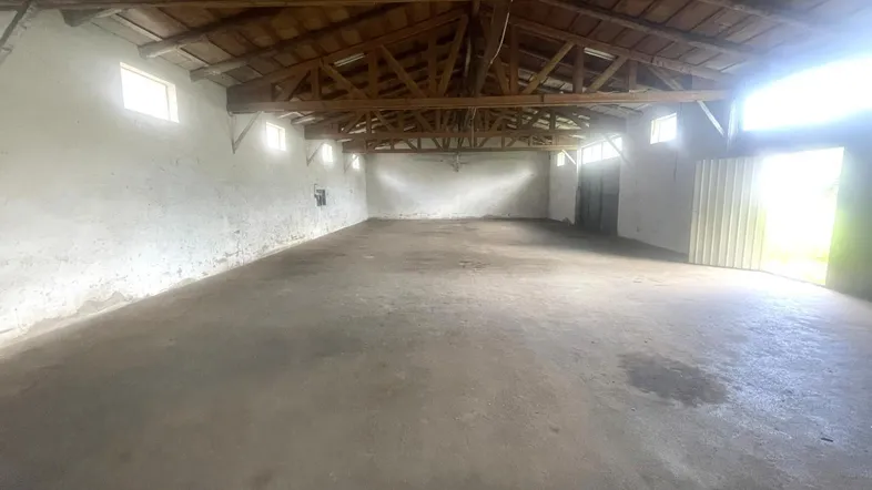 Großer, leerer Innenraum mit Betonboden und sichtbarer Holzkonstruktion des Daches.