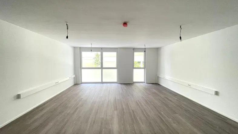 Großer, leerer Raum mit hellen Wänden und modernem Laminatboden, ideal für gewerbliche Nutzung.