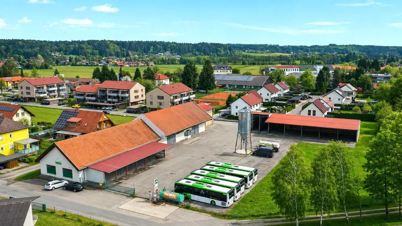 Luftaufnahme eines Gewerbeobjekts mit mehreren Gebäuden, Parkplatz und Bussen in ländlicher Umgebung.