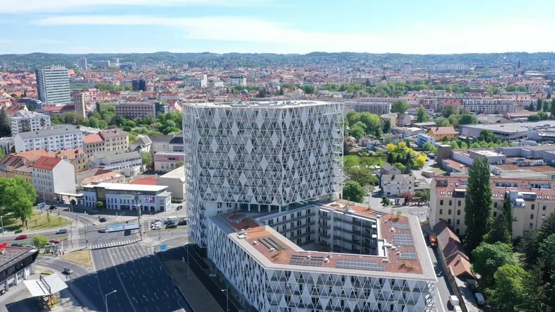 Luftaufnahme eines modernen Gebäudekomplexes mit markanter Fassadenstruktur in städtischer Umgebung.