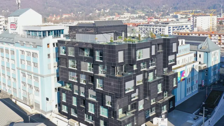 Modernes schwarzes Gebäude mit vielen Fenstern und einer komplexen Fassadenstruktur in städtischer Umgebung.