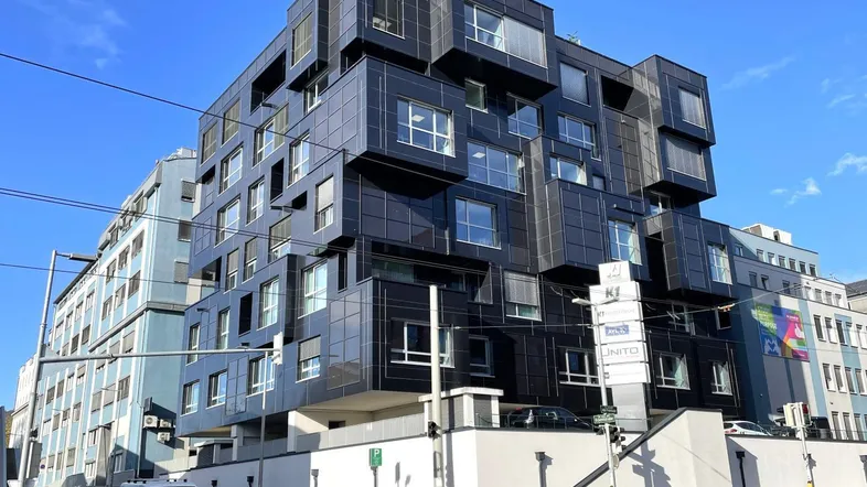 Moderne, dunkle Fassade eines Bürogebäudes mit vielen Fenstern und komplexer Architektur an einer Straße.