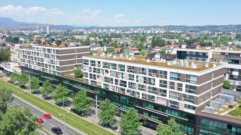 Luftaufnahme eines modernen Wohn- und Geschäftskomplexes mit begrünten Dächern und einer belebten Straße.