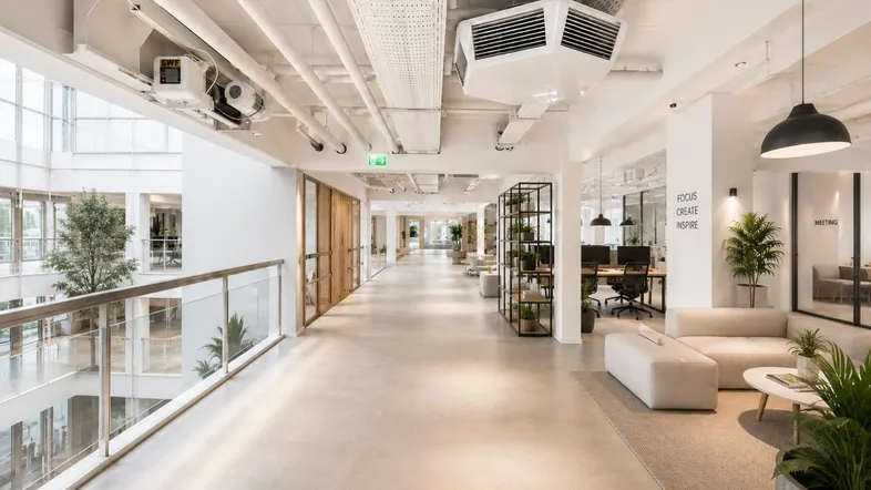 Moderner offener Bürobereich mit freiliegenden Deckeninstallationen, Betonboden und viel Tageslicht.
