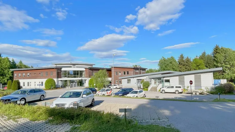 Außenansicht eines modernen Geschäftsgebäudes mit großem Parkplatz und umgebender Grünfläche unter blauem Himmel.