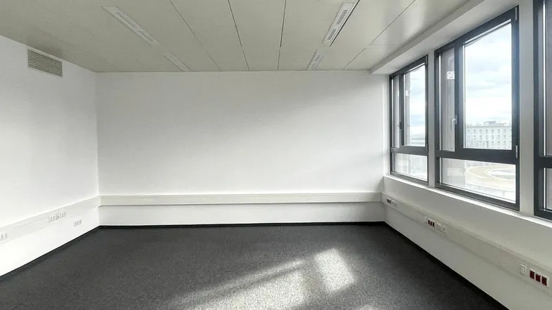Leerer Büroraum mit großen Fenstern, die viel Tageslicht hereinlassen und einen weiten Blick bieten.