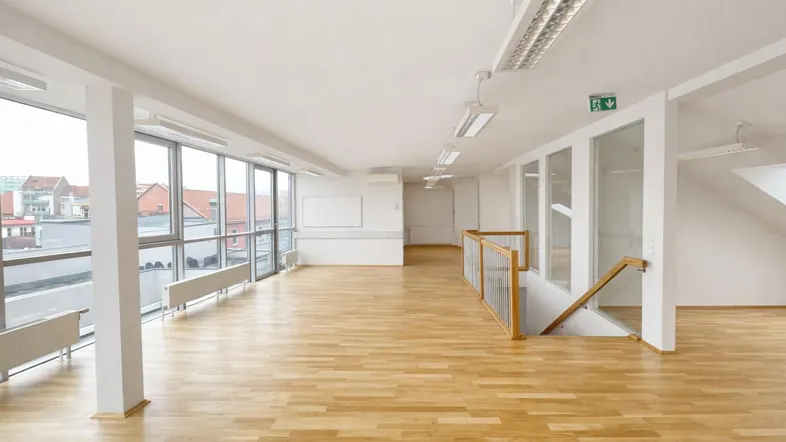 Heller, geräumiger Büroraum mit großen Fenstern, Holzboden und einer Treppe, die in eine untere Etage führt.