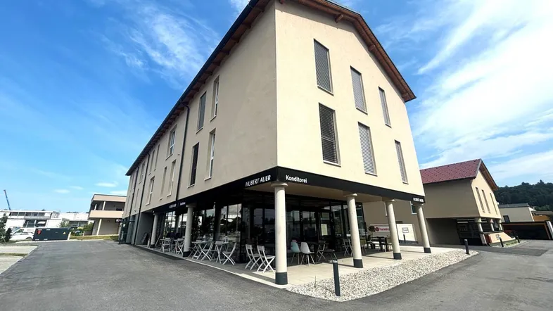 Modernes Geschäftsgebäude mit Café im Erdgeschoss und Außenbestuhlung unter einem Vordach.
