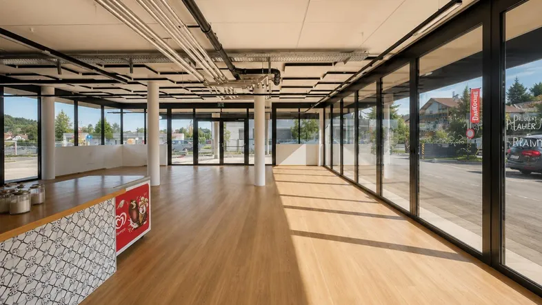 Großer, heller Gewerberaum mit vielen Fenstern, Holzboden und moderner Deckenkonstruktion, ideal für Einzelhandel.