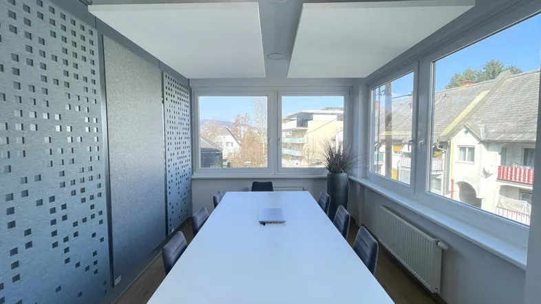Heller Konferenzraum mit großem Tisch, bequemen Stühlen und schallabsorbierenden Paneelen an Wand und Decke.