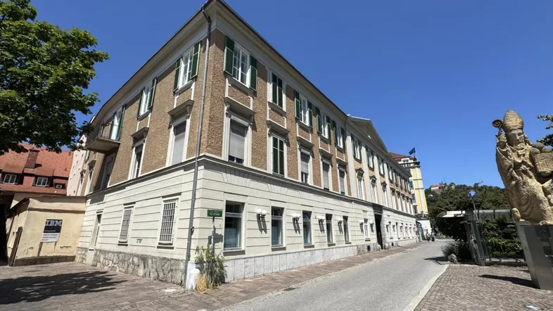 Historisches Gebäude mit klassischer Fassade, grünen Fensterläden und einem Balkon an einer städtischen Straße.