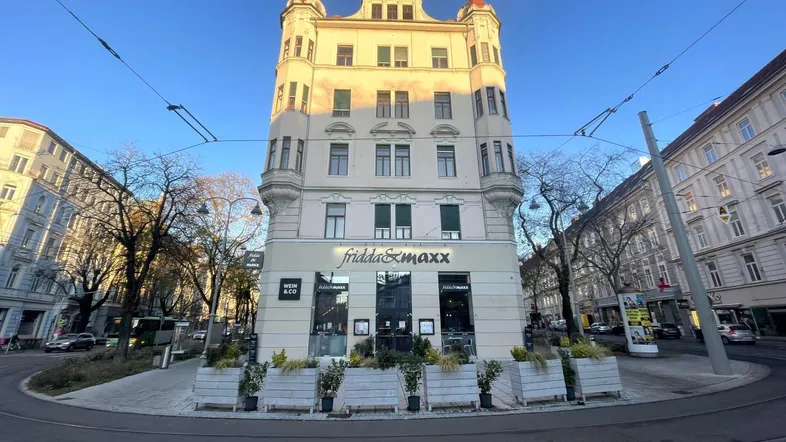 Historisches Eckgebäude mit markanter Architektur und Geschäften im Erdgeschoss an einer belebten Straße.