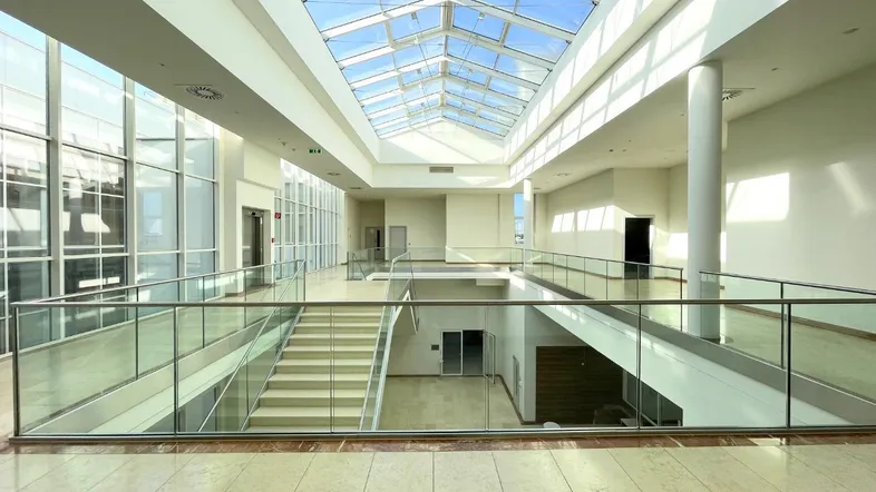 Helles, mehrstöckiges Atrium mit Glasdach und Treppe, das viel Tageslicht hereinlässt.