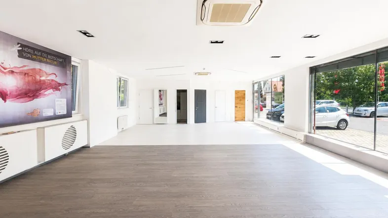Großer, heller Gewerberaum mit großen Schaufenstern, modernem Holzboden und integrierter Klimaanlage an der Decke.