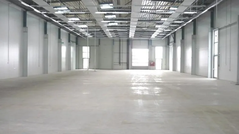 Geräumige, leere Lagerhalle mit hohen Decken, Betonboden und natürlichem Lichteinfall durch Oberlichter.
