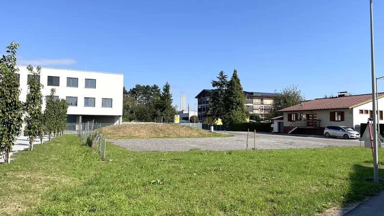 Blick auf ein unbebautes Grundstück mit Grasfläche und umliegenden Gebäuden unter blauem Himmel.