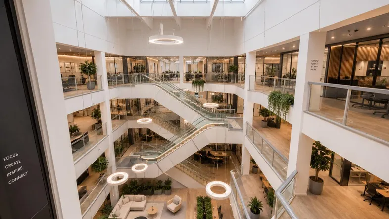 Großes, helles Atrium mit mehreren Etagen, modernen Büros, Treppen und viel Tageslicht durch das Glasdach.