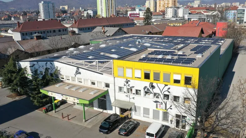 Luftaufnahme eines Gewerbegebäudes mit Solaranlage auf dem Dach und städtischer Umgebung.