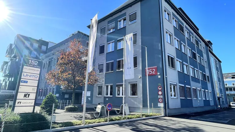 Modernes Bürogebäude mit blauer Fassade und großen Fenstern unter strahlend blauem Himmel.