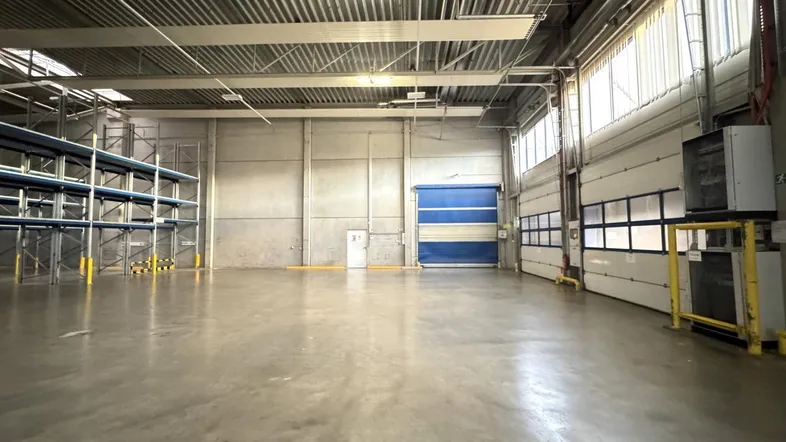 Geräumige Lagerhalle mit hohen Decken, Betonboden und großen Rolltoren für den Zugang.