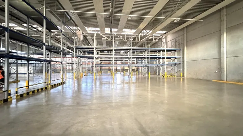 Geräumige Lagerhalle mit hohen Decken, Betonboden und umfangreichen Regalsystemen für industrielle Nutzung.
