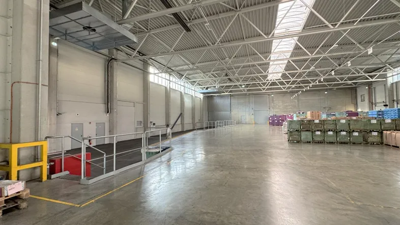 Geräumige Lagerhalle mit hoher Decke, Betonboden und viel Tageslicht durch Oberlichter und Fenster.
