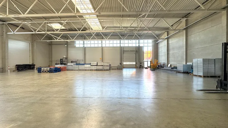 Geräumige Lagerhalle mit hoher Decke, Oberlichtern und Betonboden, bereit für die Nutzung.