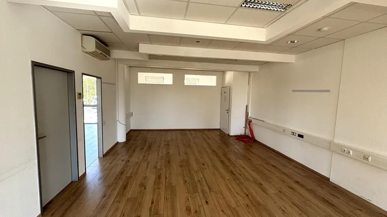 Geräumiger, leerer Büroraum mit hellem Holzfußboden, abgehängter Decke und Klimaanlage.