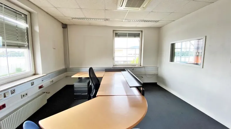 Geräumiges Büro mit Schreibtisch, Bürostuhl, Fenstern und Klimaanlage, ideal für konzentriertes Arbeiten.
