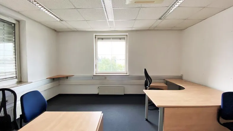 Helles Büro mit Teppichboden, Schreibtischen und Klimaanlage an der Decke.