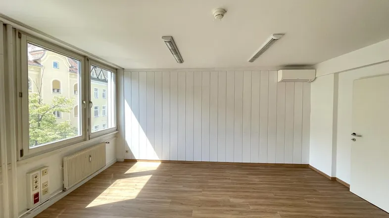 Heller Büroraum mit großen Fenstern, Laminatboden und Klimaanlage, ideal für produktives Arbeiten.