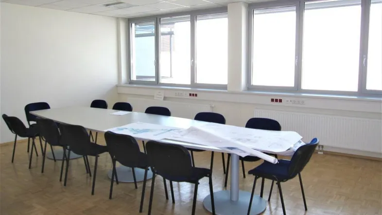 Geräumiger Konferenzraum mit großem Tisch, vielen Stühlen und hellen Fenstern, ideal für Besprechungen.