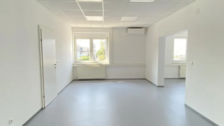 Heller, leerer Büroraum mit großen Fenstern, Klimaanlage und abgehängter Decke.