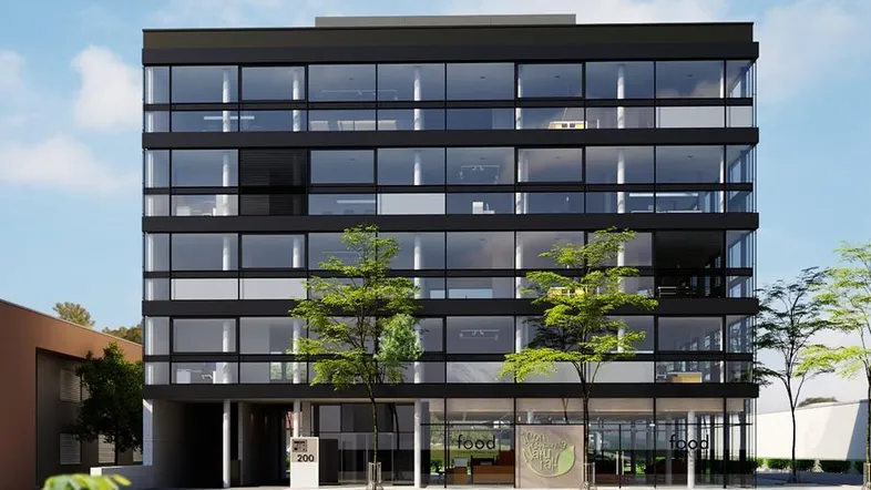 Modernes Geschäftsgebäude mit schwarzer Fassade und großen Glasflächen, umgeben von Bäumen und einer Straße.
