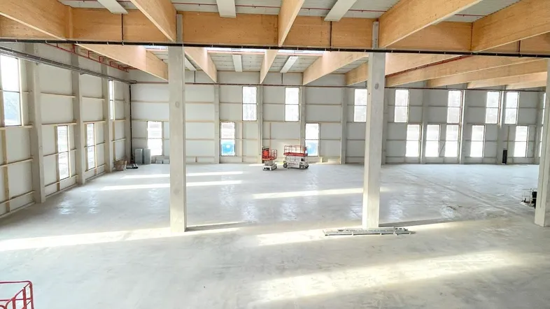 Großer, leerer Lagerraum mit hohen Decken, Holzbalken und vielen Fenstern, bereit für den Ausbau.