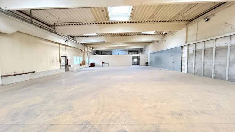 Geräumige, leere Lagerhalle mit hohen Decken, Oberlichtern und robustem Betonboden, bereit zur Nutzung.
