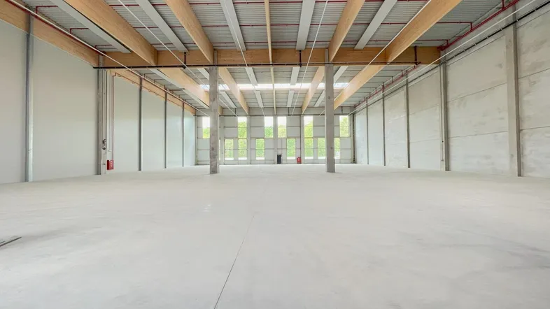 Geräumige, leere Lagerhalle mit hohen Decken, sichtbaren Holzbalken und großen Fenstern, die viel Tageslicht hereinlassen.