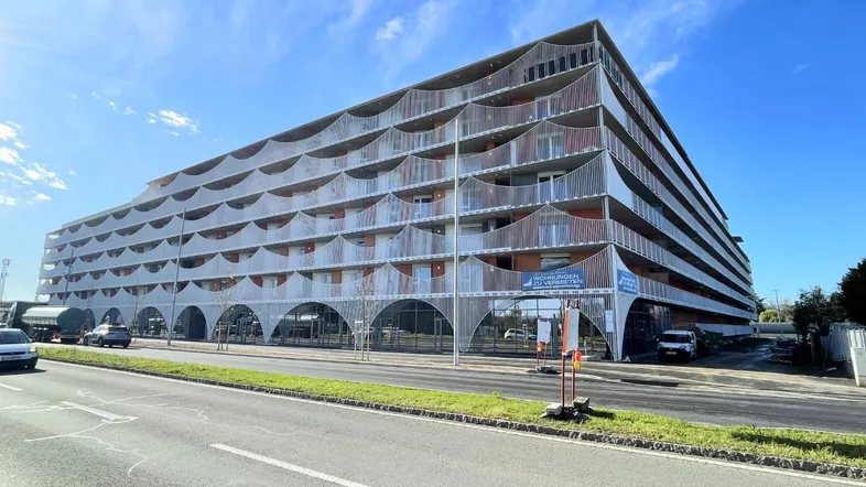 Modernes Mehrfamilienhaus mit vielen Balkonen und einer auffälligen wellenförmigen Fassadengestaltung an einer Straße.