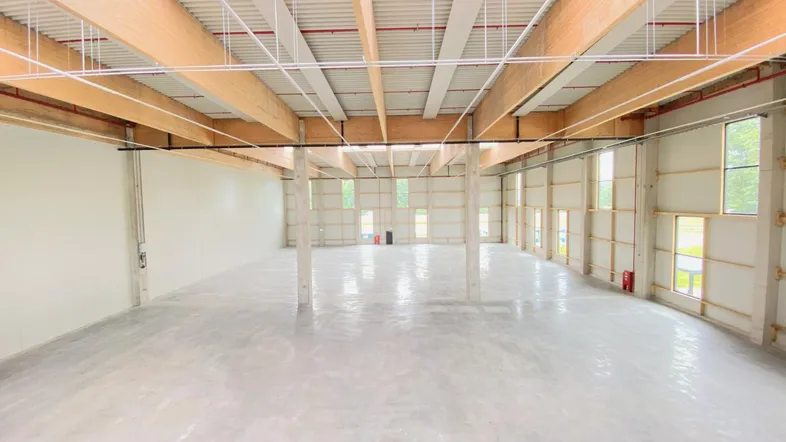 Geräumige, leere Lagerhalle mit hohen Decken, Holzbalken und Betonboden, bereit zur Nutzung.