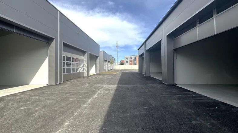 Außenansicht mehrerer moderner Lagerhallen mit großen Rolltoren und asphaltierter Zufahrt unter blauem Himmel.
