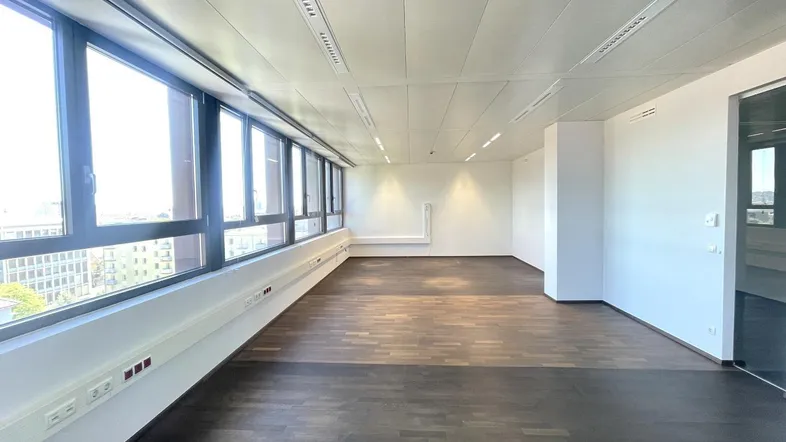 Geräumiges Büro mit großen Fenstern, dunklem Holzboden und viel Tageslicht, ideal für moderne Arbeitsumgebungen.