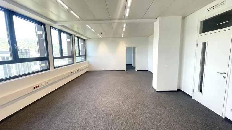 Großes, helles Büro mit Teppichboden, vielen Fenstern und Zugang zu weiteren Räumen.