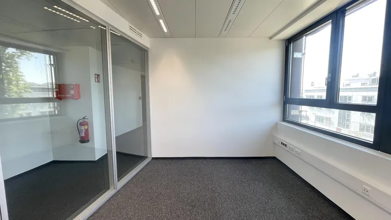 Helles Büro mit Teppichboden und einer modernen Glasabtrennung zu einem Nebenraum.