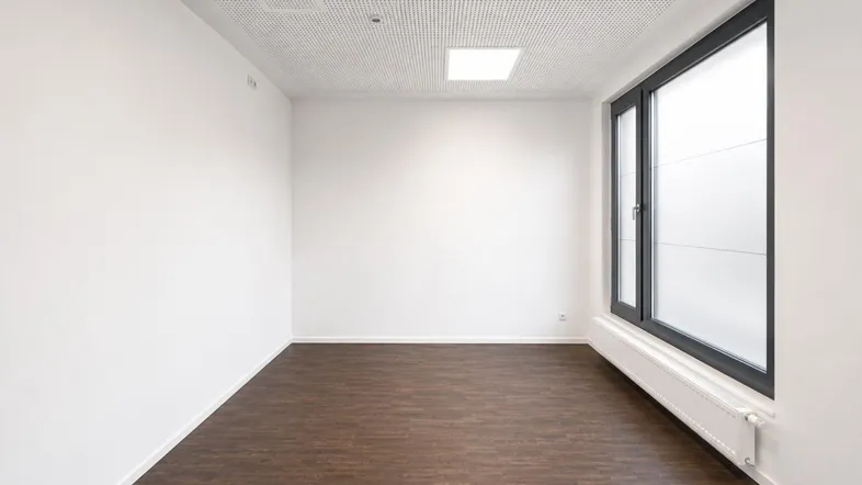Heller, leerer Raum mit großen Fenstern, dunklem Laminatboden und weiß gestrichenen Wänden, ideal für Büro oder Gewerbe.
