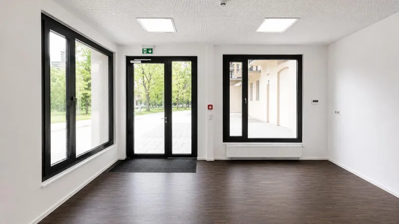Heller Eingangsbereich mit großen Fenstern, dunklem Laminatboden und weiß gestrichenen Wänden.