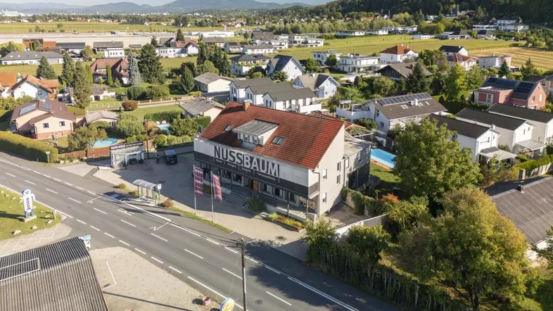 Luftaufnahme eines Gewerbegebäudes mit umliegenden Wohnhäusern und grüner Landschaft im Hintergrund.
