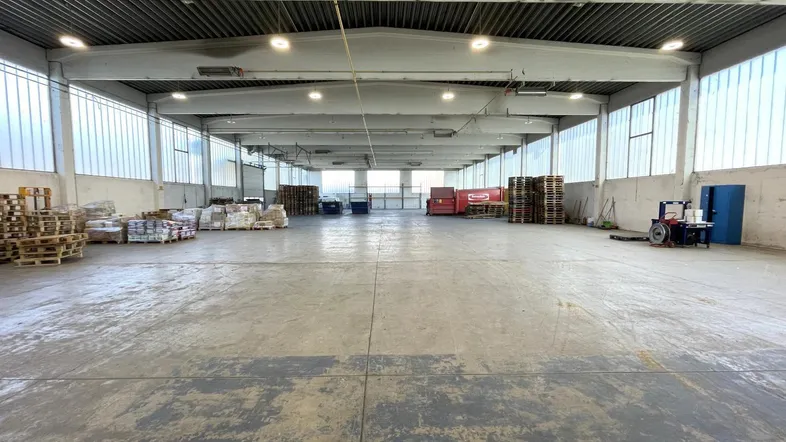 Geräumige Lagerhalle mit Betonboden, hohen Decken und Tageslicht durch Oberlichter an den Wänden.