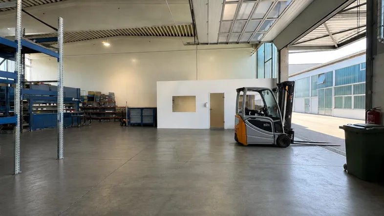 Geräumige Lagerhalle mit Betonboden, hohen Decken und einem Gabelstapler, bereit zur Nutzung.