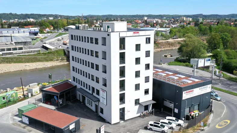 Luftaufnahme eines modernen weißen Bürogebäudes mit umliegenden Gewerbeflächen und Flussblick.